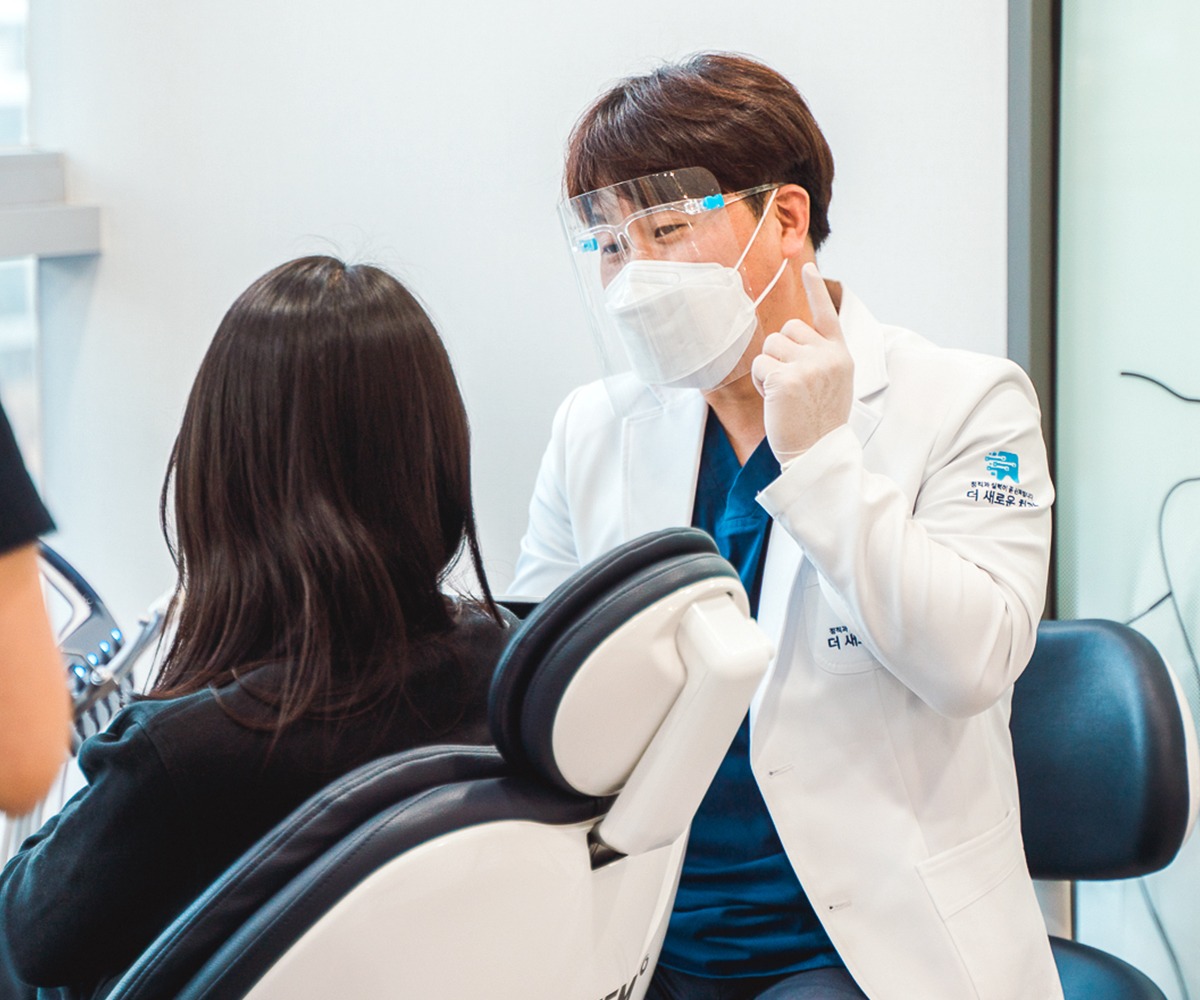 강민구 대표원장이 진료 의자에 앉은 환자를 마주 보고 손짓으로 설명하고 있다
